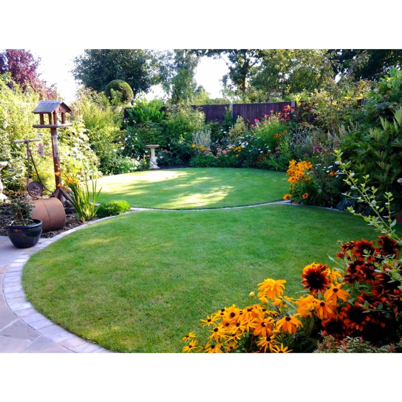 Curved lawn framed by deep borders of rudbeckia and shrubs, with a bird table and birdbath